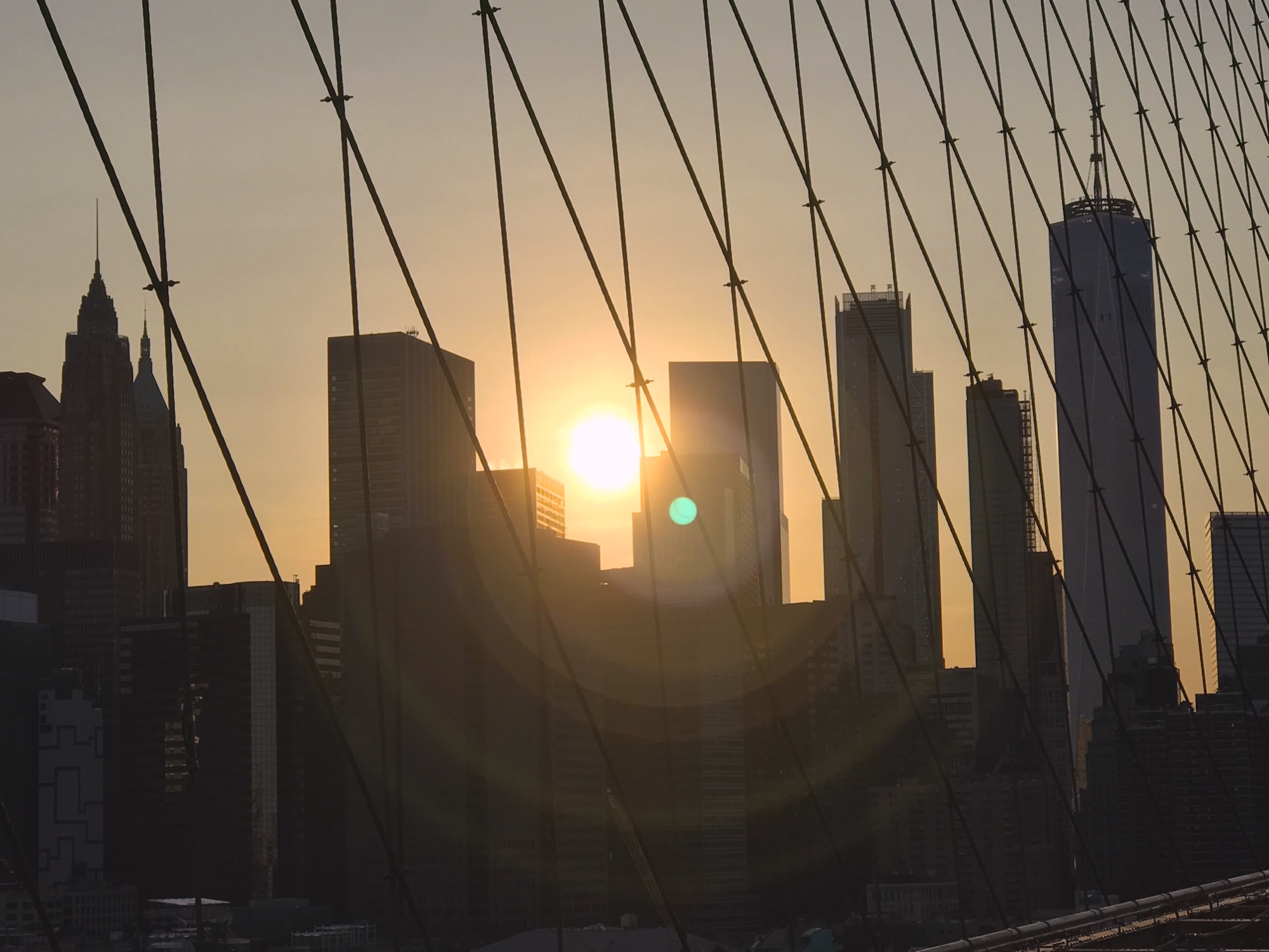 Photo of sunset over Manhattan seen from Brooklyn Bridge.